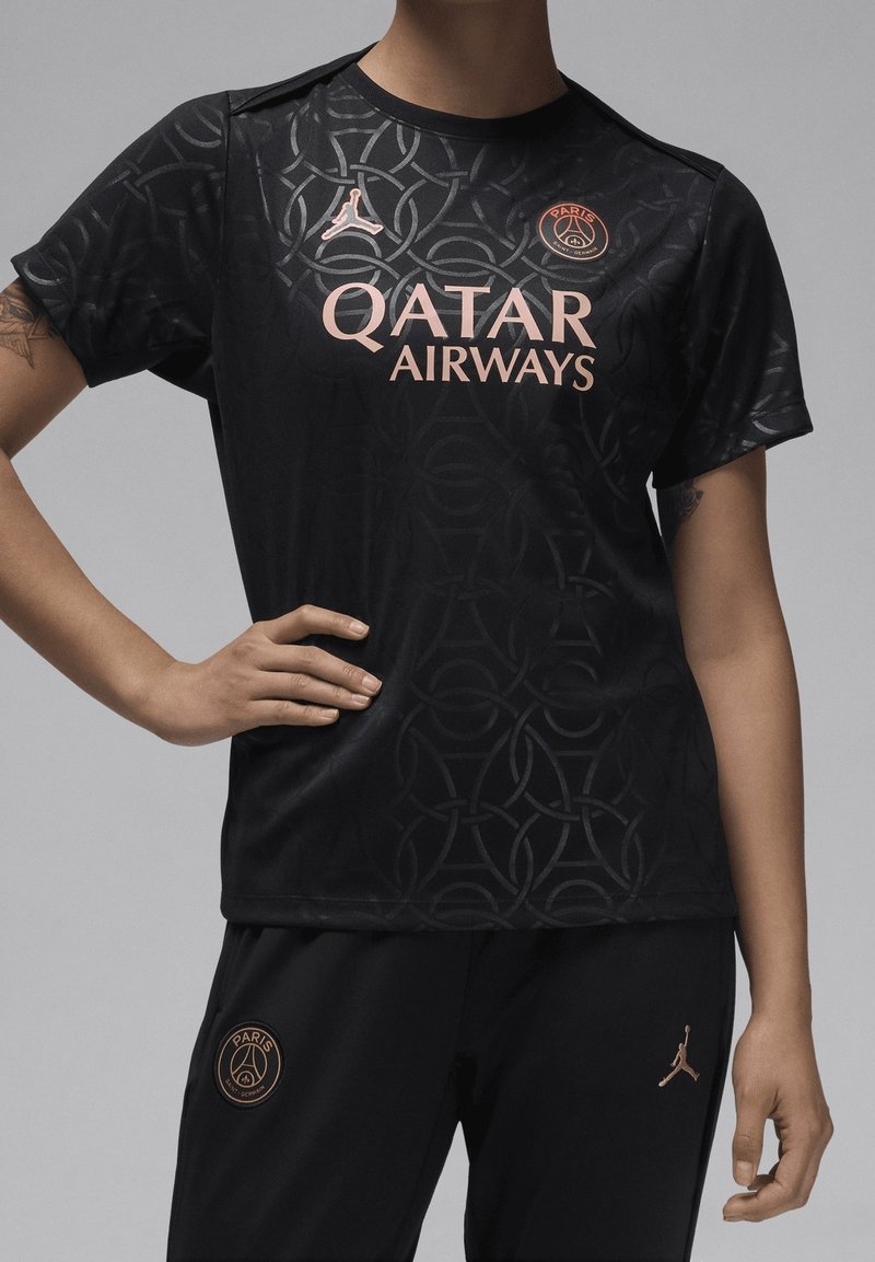 Camiseta deportiva negra con un patrón circular texturizado, que presenta un logo rosa de Qatar Airways y PSG, complementada por pantalones negros con detalles en dorado.