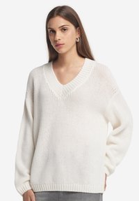 Vit stickad tröja med V-ringning, avslappnad passform och lång ärm, med en texturerad yta samt ribbade muddar och nederkant.