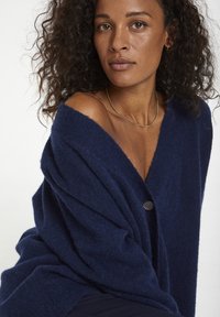 Marinblå oversized cardigan i mjukt stickat material med djup V-hals, knappp detaljer och avslappnad passform med texturerad yta.