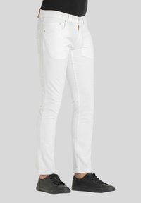 Jeans in denim bianco con vestibilità slim, dotati di tasche anteriori e posteriori e hardware della cerniera in tonalità dorata. Abbinati a sneakers nere.