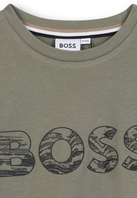Olijfgroene T-shirt met ronde hals; heeft een textuur, grafisch "BOSS"-logo in donkergrijs; de stof lijkt glad en lichtgewicht.