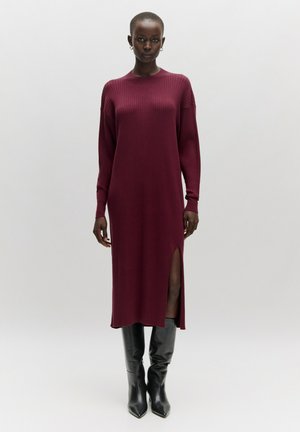 Burgunderfarbendes, geripptes Strick-Midikleid mit langen Ärmeln, seitlichem Schlitz und Rundhalsausschnitt, kombiniert mit schwarz-weißen Knöchelstiefeln mit spitzem Design.
