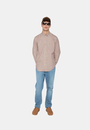 Chemise à carreaux orange et bleu, jeans bleu clair, chaussures marron et lunettes de soleil ; le mannequin se tient les mains dans les poches.