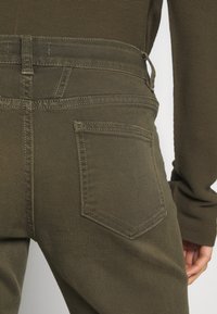 Jeans en denim vert olive avec une coupe ajustée, des poches arrière renforcées par des coutures solides et une texture lisse.