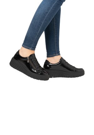 Baskets en cuir verni noir avec semelle en caoutchouc texturée, présentant un laçage à l'avant et un détail de fermeture éclair sur le côté. Portées avec un jean skinny bleu.