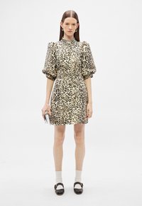 Sukienka w panterkę z krótkimi bufiastymi rękawami, wysokim kołnierzem, dopasowaną talią i rozkloszowanym dołem. Tkanina ma gładką, błyszczącą strukturę.