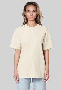 T-shirt en coton beige à manches courtes et col rond, avec une coupe décontractée et des détails minimaux. Associé à un jean bleu clair.