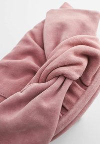 Soft pink fabric wrap with a smooth texture, featuring a twisted design and visible stitching along the edges, creating a layered appearance.