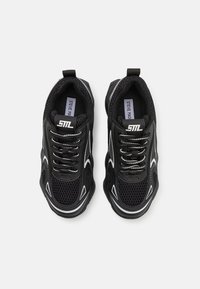 Zapatillas deportivas negras con parte superior de malla, detalles en blanco y cordones en contraste. Diseñadas con punta redondeada y cuello acolchado para mayor comodidad.