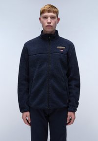 Marineblaue Fleecejacke mit hohem Kragen, durchgehendem Reißverschluss und strukturierter Oberfläche. Fällt auf durch ein Logo-Patch und seitliche Taschen.