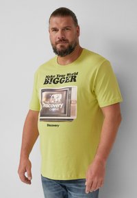 Żółta koszulka t-shirt z krótkim rękawem z grafiką retro telewizora. Napis brzmi "Rozszerz swój świat" oraz "Discovery Channel."
