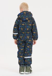 Blauw en groen dinosaurussen-patroon sneeuwpak, met een capuchon en reflecterende accenten, gecombineerd met grijze winterlaarzen.