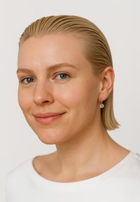 Guldörhänge med blommönster; modellen har rakt, slickat blont hår och bär en rundhalsad vit topp. Slät hudtextur.