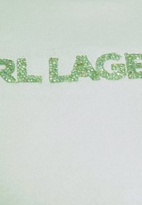 Tachuelas verdes dispuestas para formar las palabras "RL LAGER" sobre un fondo de tela blanca acanalada.