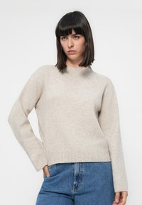 Beige kötött pulóver bordás szegéllyel és kerek nyakkal. Hosszú ujjú, laza szabású, puha textúrájú anyagból készült.