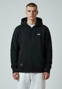 Hoodie noir zippé en mélange de coton, doté d'une poche avant, d'une capuche avec cordon de serrage et d'un petit logo blanc sur la poitrine.