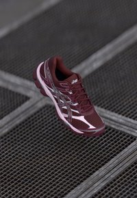 Bordo tekaški čevljek z mrežastim zgornjim delom, kontrastnimi roza detajli in odsevnimi elementi. Ima oblazinjen podplat in vezalni odprtina.