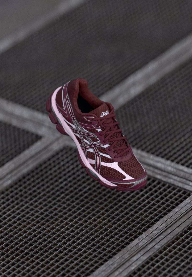 Bordo tekaški čevljek z mrežastim zgornjim delom, kontrastnimi roza detajli in odsevnimi elementi. Ima oblazinjen podplat in vezalni odprtina.