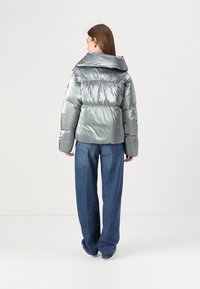 Casaco puffer prateado metálico com colarinho alto, cintura ajustada e mangas compridas, combinado com jeans de perna larga azul claro.