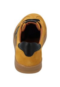 Sneaker giallo in suede con accenti neri, forma arrotondata e fodera beige. Presenta un colletto imbottito, dettagli cuciti e suola in gomma.