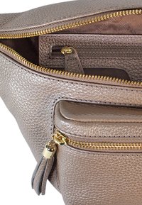 Interno di una borsa in pelle grigia testurizzata con zip dorata, dotata di una piccola tasca e un dettaglio con frange. Design pulito con scomparti funzionali.