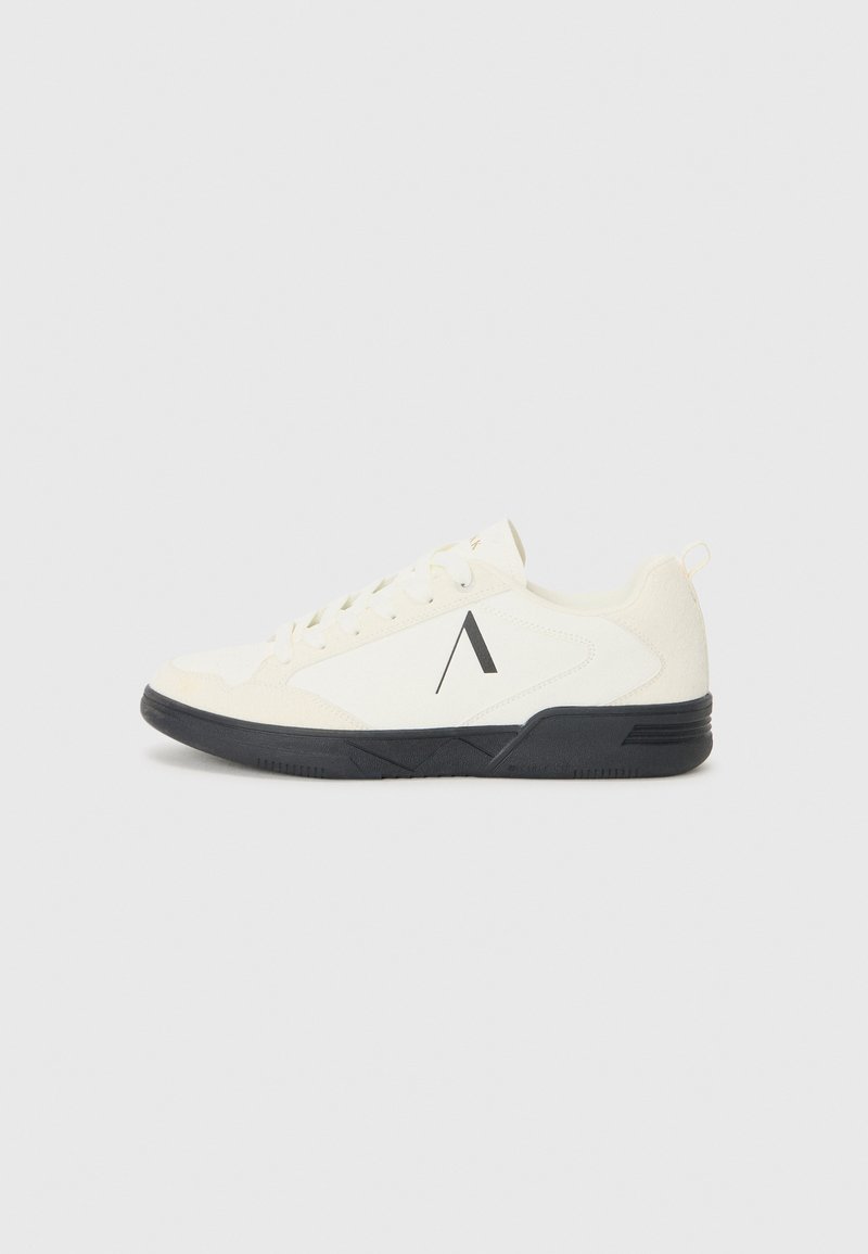 Zapatilla deportiva blanca con un upper texturizado, suela negra y un acento geométrico en el costado. Los cordones con un diseño plano y redondeado completan el aspecto.