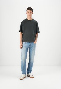 Czarnoszary, oversize t-shirt, jasnoniebieskie dżinsy i białe trampki. Tatuaż widoczny na lewym ramieniu. Prosty, casualowy styl z luźnym krojem.