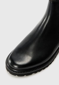 Black leather boot with a smooth finish, rounded toe, and a textured rubber sole featuring a ridged edge.