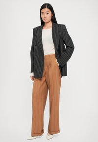 Černé oversized sako s jemným proužkem a dvěma knoflíky, béžový úzký top a široké kalhoty v tan barvě se shodnými proužky. Špičaté bílé lodičky.