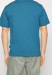 Teal tričko s krátkým rukávem vyrobené z bavlny, s kulatým výstřihem a rovnými lemy. Na zadní straně je čistý design bez viditelných log.