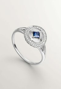 Anillo de plata con una piedra azul cuadrada en el centro, rodeada por un halo de pequeñas piedras claras y un diseño circular texturizado.