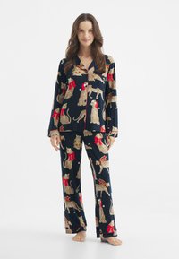 Granatowy zestaw piżamowy z długim rękawem i spodniami, z motywem lamparta w czerwonych i zielonych akcentach. Gładki materiał, luźny krój.