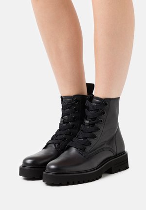 Botas de cuero negras hasta el tobillo con punteras redondas, cordones negros y costados texturizados. Suelas de goma gruesas con relieves para mayor tracción.