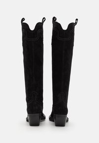 Black suede over-the-knee boots with a scalloped top, decorative stitching, and small pull tabs. Block heel and smooth texture.