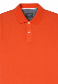 Polo arancione con colletto classico, patta con due bottoni e tessuto testurizzato. Presenta un dettaglio a contrasto nella banda interna del colletto.