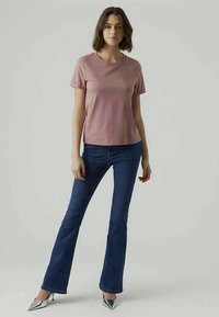 Light pink crew-neck t-shirt paired with blue flared jeans and pointed silver heels. Smooth fabric texture with a relaxed fit.