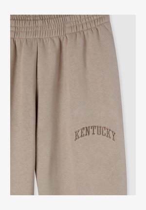 Pantaloni della tuta beige con elastico in vita e testo ricamato "KENTUCKY" in una tonalità più scura. Tessuto morbido e liscio.