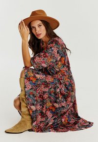 Kwiatowa długa sukienka w ciemnych tonach z różowymi, pomarańczowymi i niebieskimi kwiatami; luźny krój, miękki materiał. W połączeniu z beżowym filcowym kapeluszem i beżowymi kozakami sięgającymi do kolan.