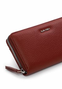 Cartera de cuero marrón texturizado con cremallera plateada y logotipo "SURI FREY" en el frente, mostrada sobre un fondo blanco.