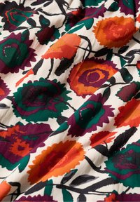 Tkanina s odvažnim cvjetnim uzorkom koja prikazuje velika narančasta, zelena, ljubičasta i crna cvijeća na bijeloj pozadini s vidljivom teksturom i naborima.