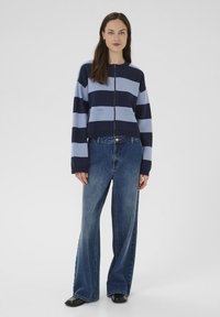 Cardigan a righe blu navy e azzurro in maglia con chiusura a zip, scollatura tonda e tasche a toppa. Abbinato a jeans in denim a gamba larga.
