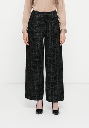 Schwarze Culottenhosen mit einem strukturierten Muster, hoch geschnitten und mit einem weißen Karodesign. Kombiniert mit schwarzen High Heels.