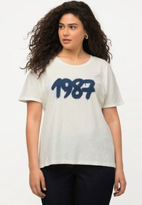 Bílý bavlněný tričko s námořnickou modrou grafikou "1987" potištěnou na přední straně. Krátké rukávy a volný střih.