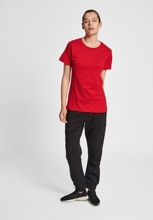 Rød bomulds t-shirt med rund halsudskæring, korte ærmer og lige kant, båret med sorte sweatpants og sorte sportsko.
