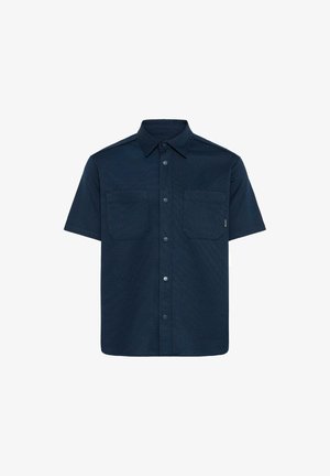Kratka srajca z dolgimi rokavi temno modre barve, z dvema prsnikoma in klasičnim ovratnikom, oblikovana iz strukturirane tkanine.