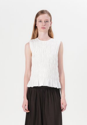 Top blanco sin mangas con un diseño texturizado de fruncido y un dobladillo con volantes. Se lleva con una falda negra y cuenta con un escote redondo.