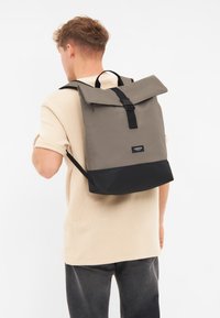 Grå rulltopp ryggsäck med svart botten, med spänne stängning och justerbara remmar. Tillverkad av slitstark tyg med en elegant design.