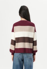 Pull en tricot avec des rayures horizontales en bordeaux, beige, crème et marron. Coupe décontractée avec des épaules abaissées et des poignets côtelés.