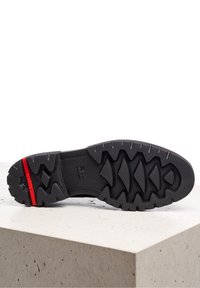 Suola di scarpa nera caratterizzata da un motivo di grip testurizzato, con un accento rosso sul tallone e un design di battistrada geometrico per la trazione.