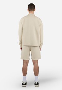 Beige textured sweatshirt and shorts set. Loose fit with dropped shoulders. Coupled with white socks and black-accented sneakers.